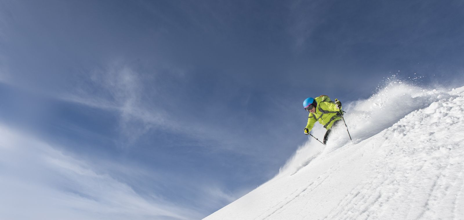 A skier carves their way down a steep mountain slope, spraying snow behind them.